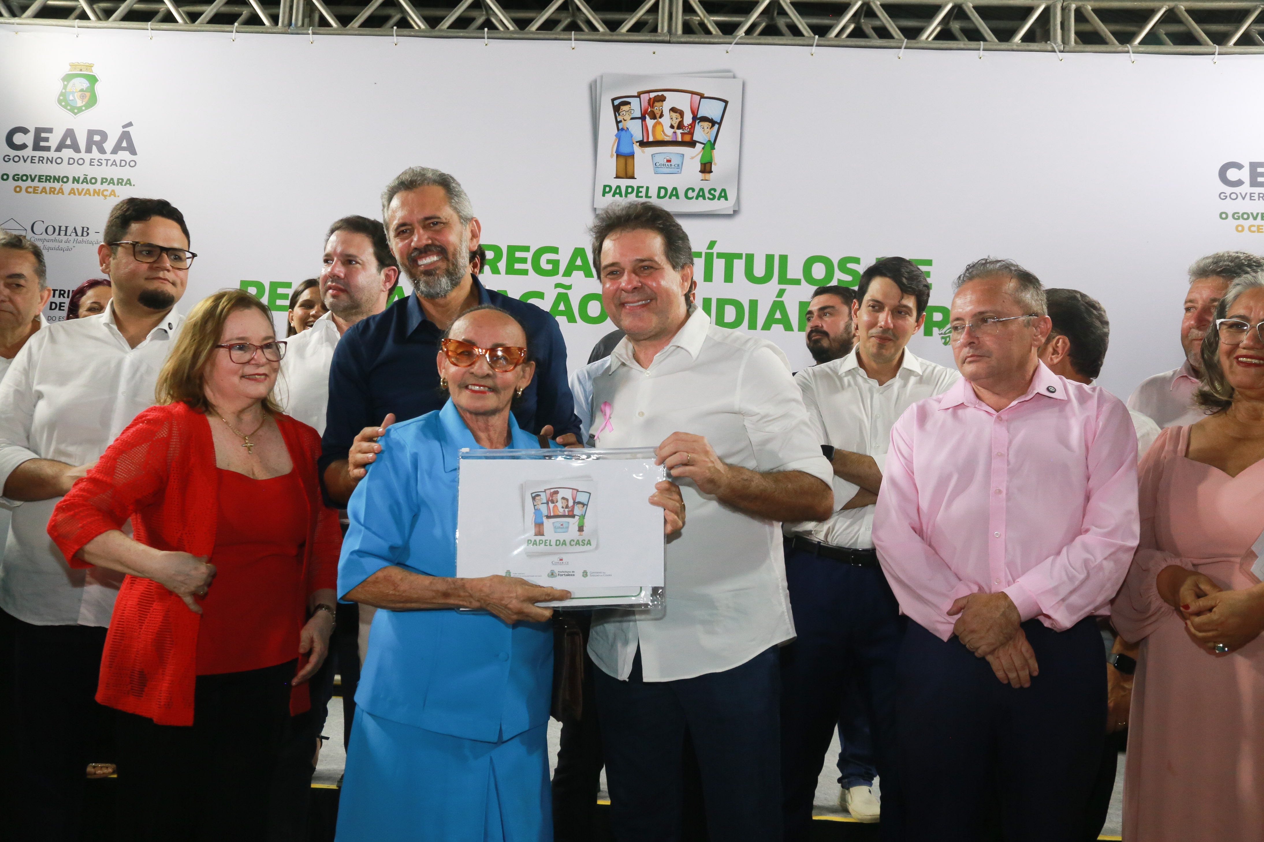 prefeito evandro posa com uma senhora no palco e entrega um documento para ela